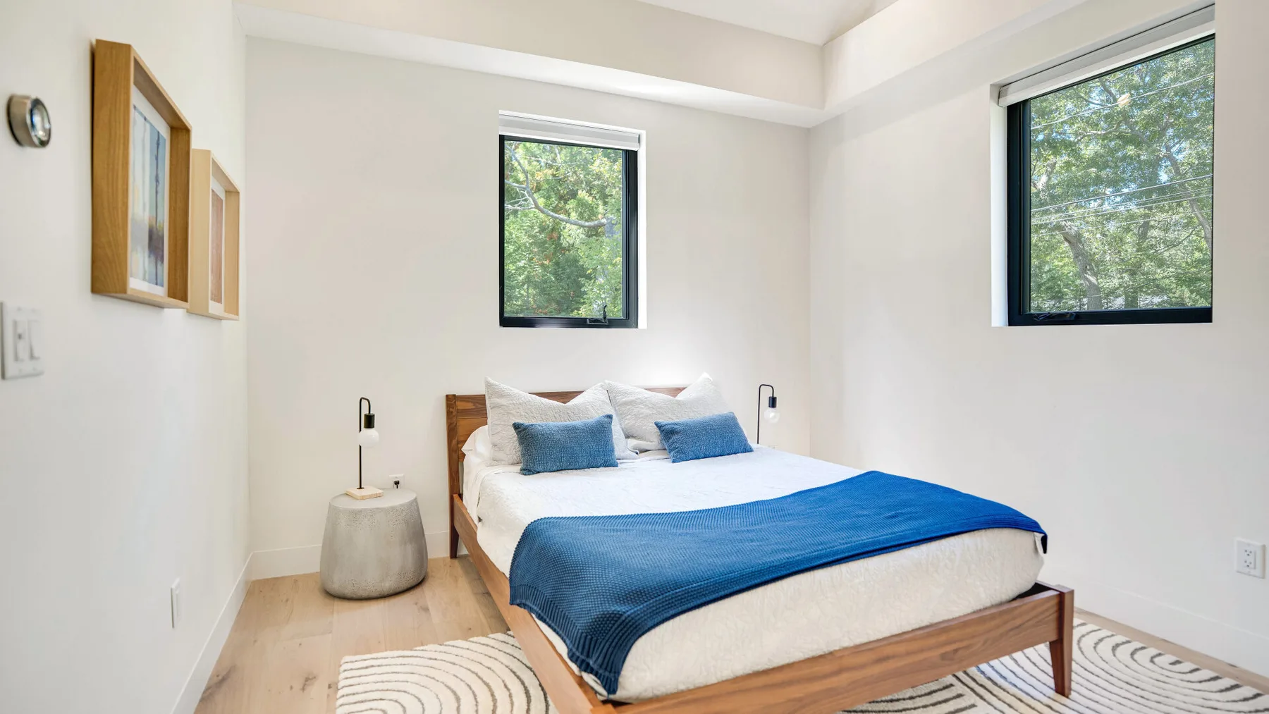 Un dormitorio luminoso con una cama vestida con ropa de cama blanca y azul.