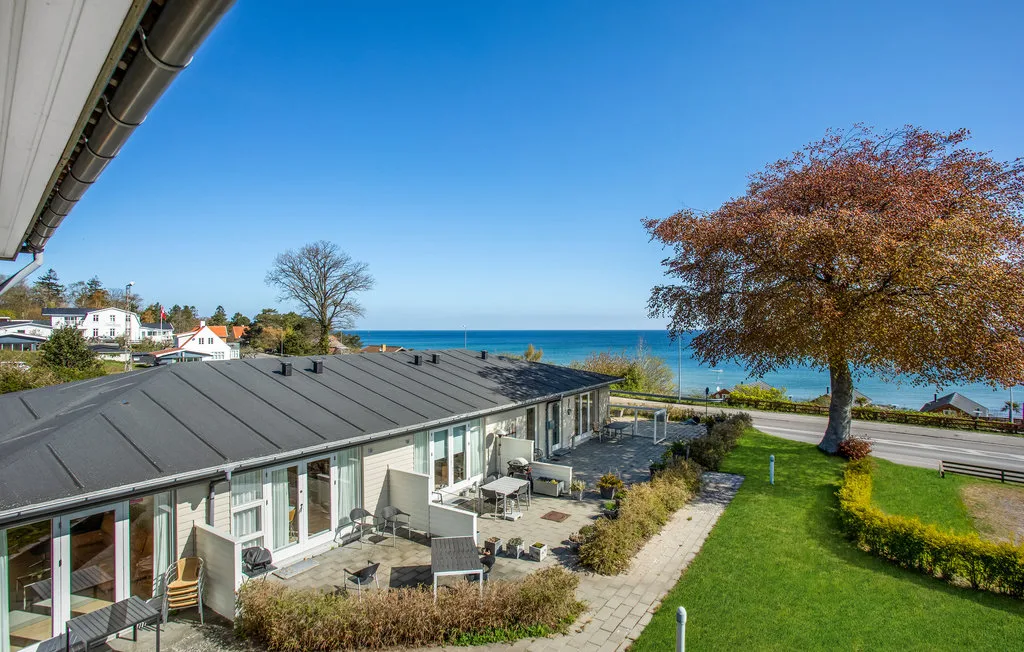 A coastal residential scene with a patio, green lawn, and the sea beyond.