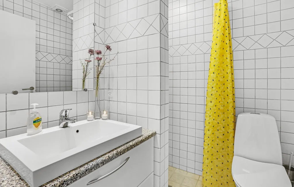 A tiled bathroom with a sink, toilet, and yellow shower curtain.