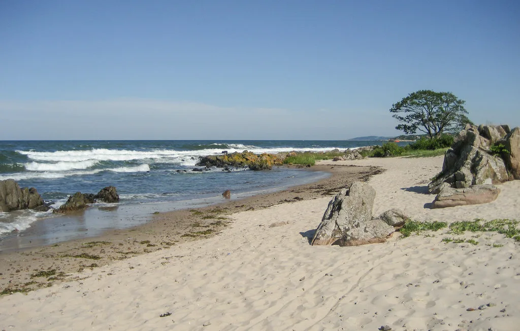 A sandy beach meets the ocean, with rocks along the shore.