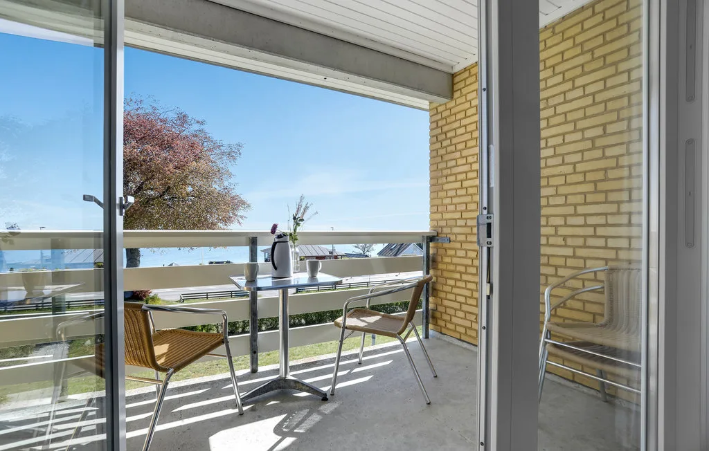 A covered balcony with a table and seating overlooks trees and the surrounding area.