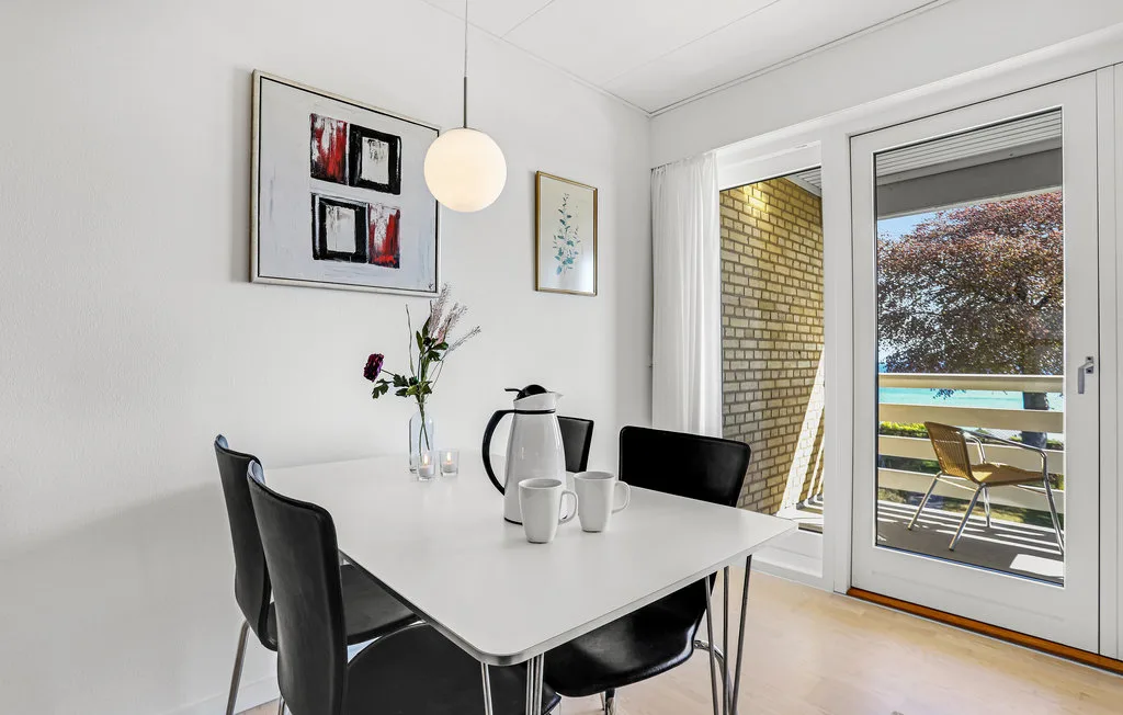 A bright dining area with a white table, dark seating, and glass doors to a balcony.
