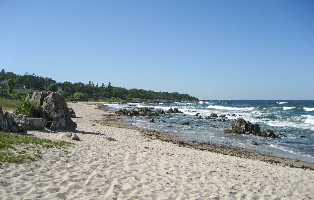 A sandy beach with rocky outcrops beside the ocean.