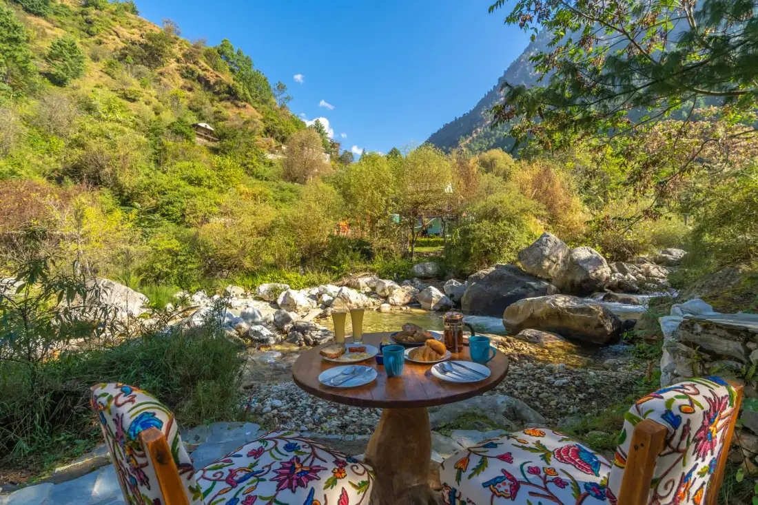 Asientos al aire libre junto a un arroyo rocoso, con una mesa pequeña entre dos sillas estampadas.