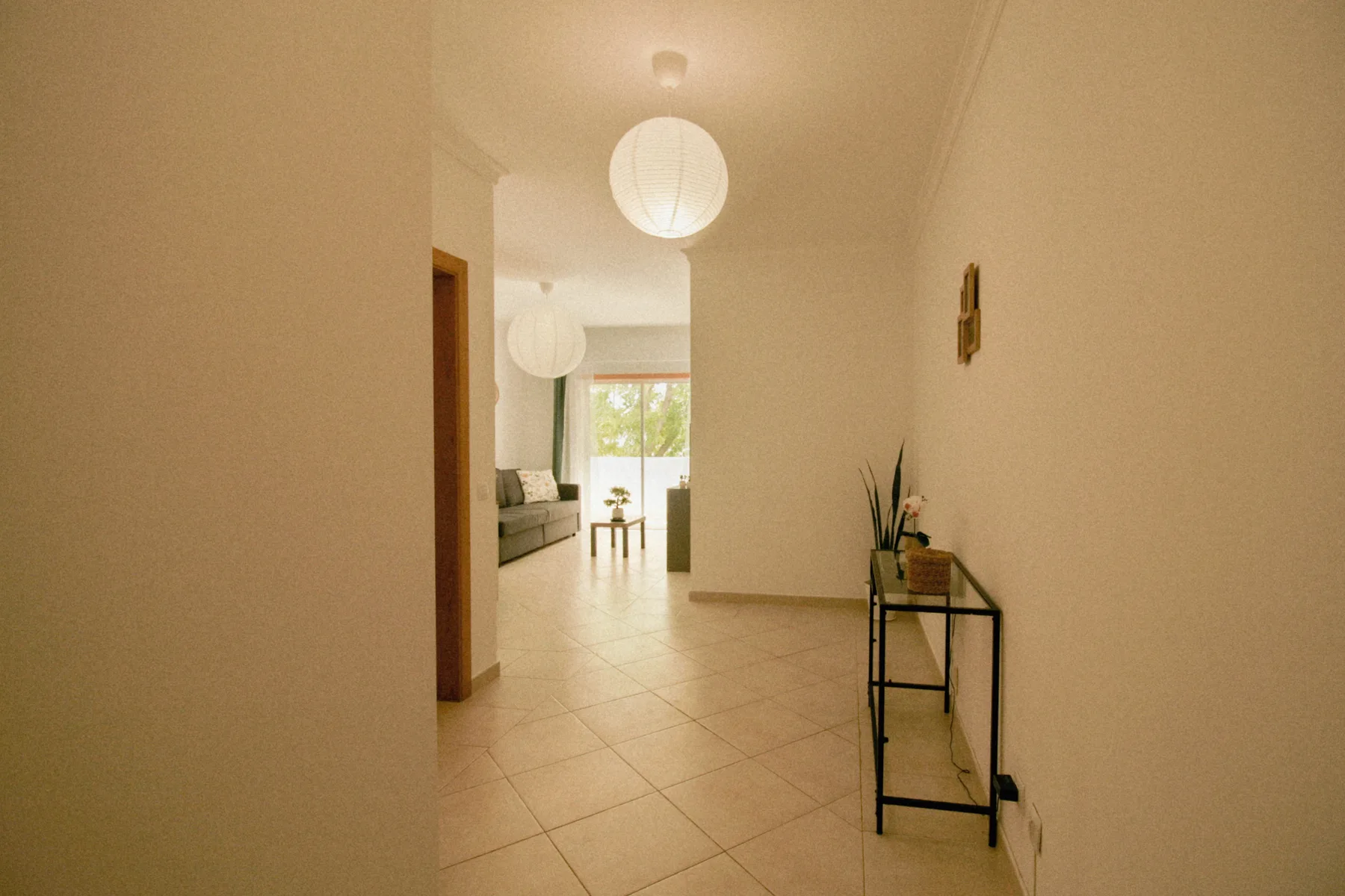 Un pasillo luminoso de apartamento se abre a una sala de estar con una mesa pequeña.