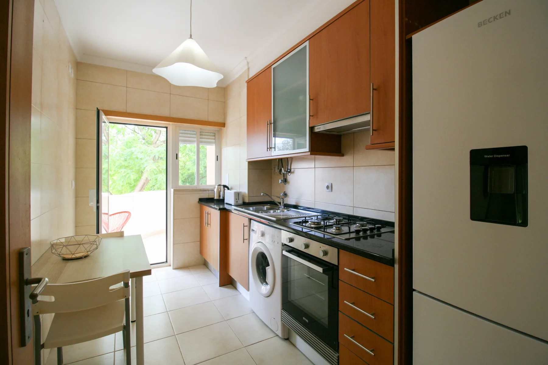 Una cocina luminosa con armarios de madera, electrodomésticos y una pequeña mesa de comedor.
