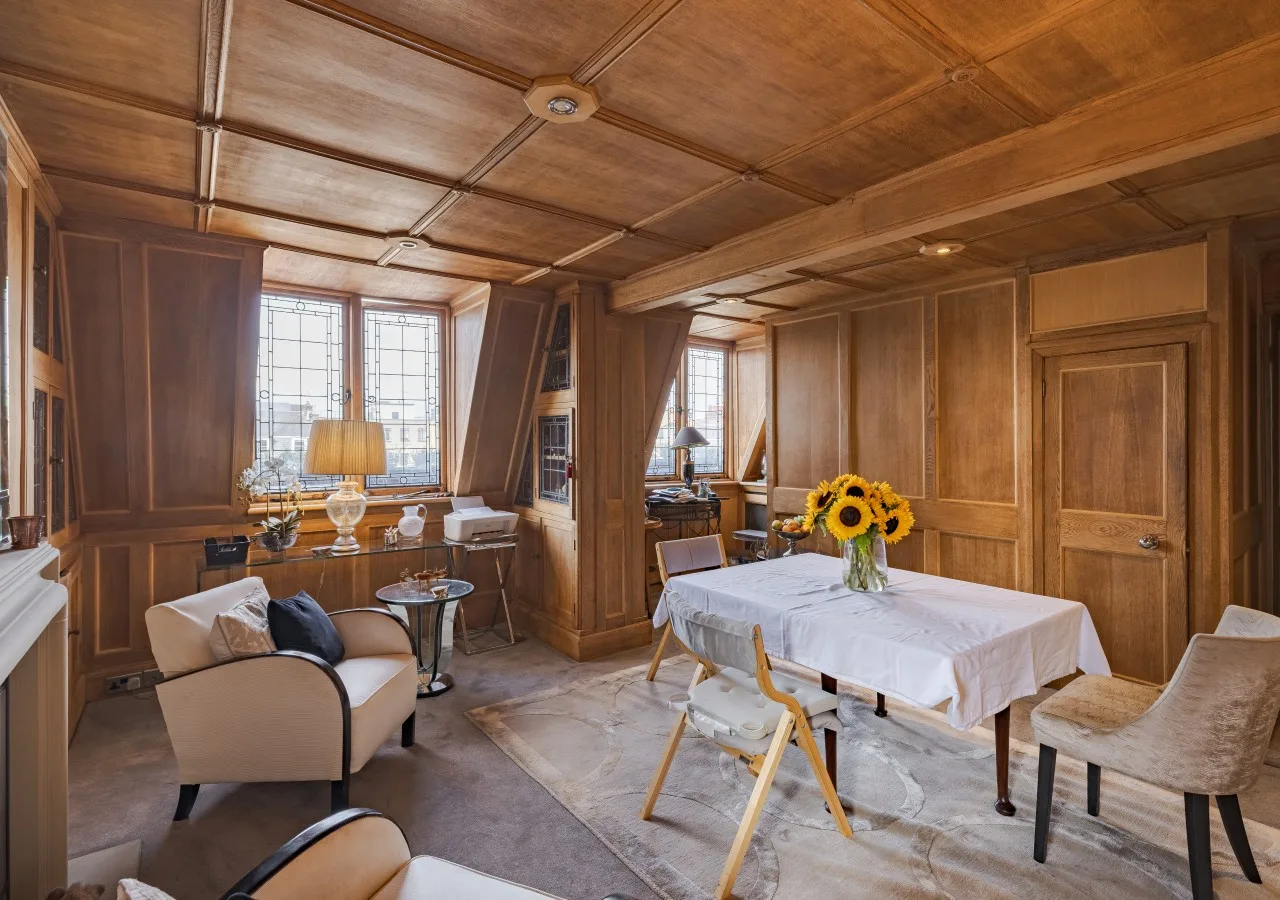 Una habitación con paneles de madera, mesa de comedor y asientos junto a grandes ventanas.