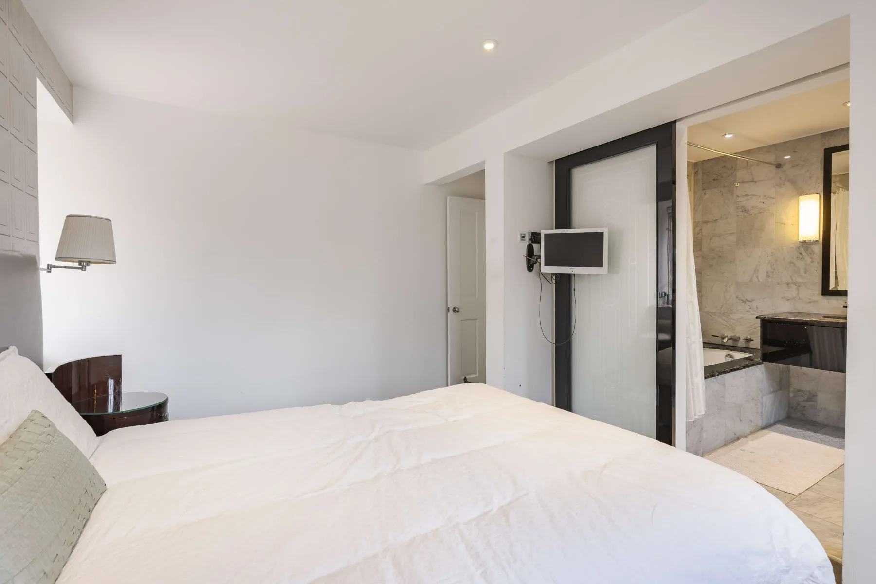 Un dormitorio luminoso con una cama junto a un baño abierto.