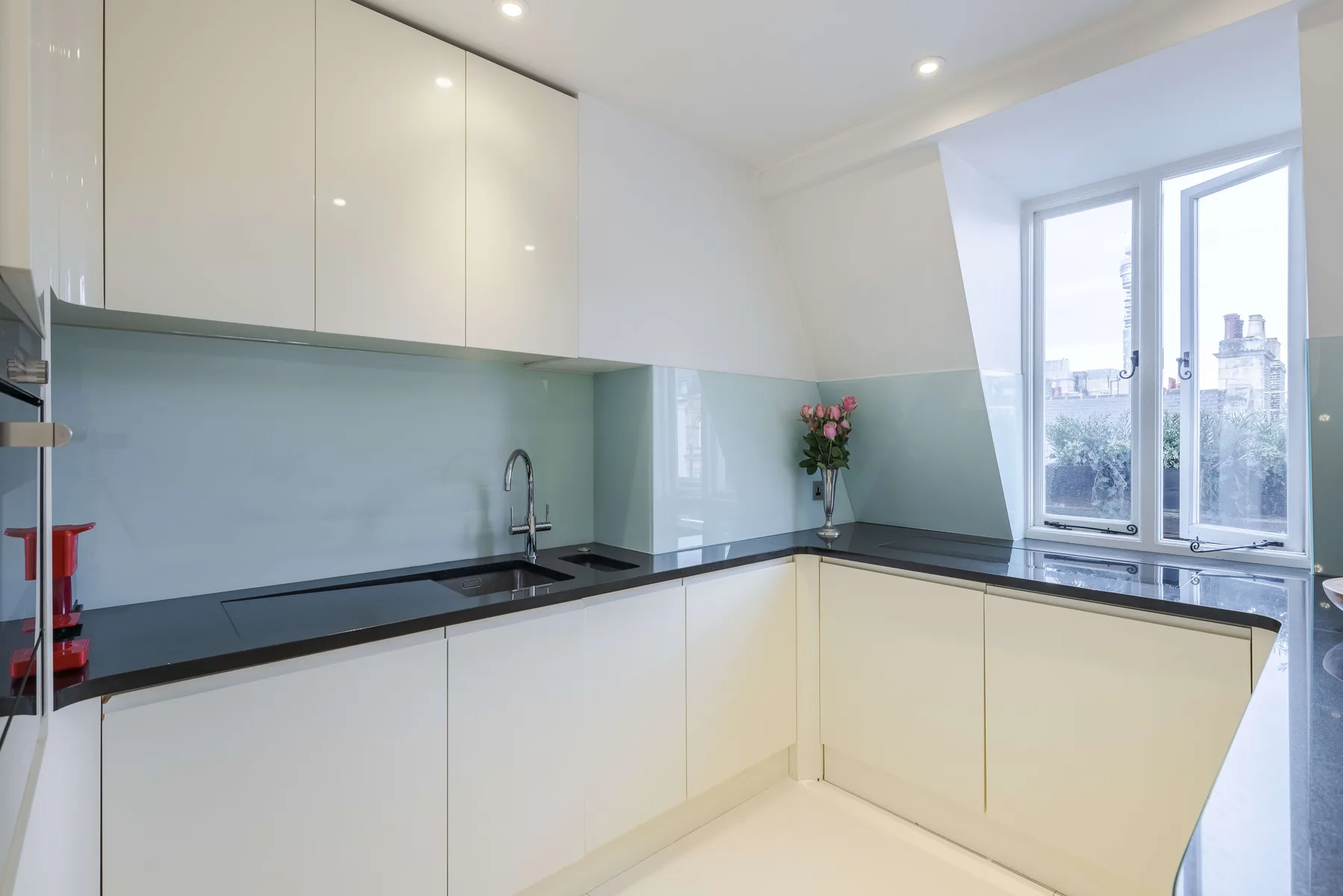 Una cocina moderna y luminosa con gabinetes blancos, encimeras oscuras y ventanas grandes.