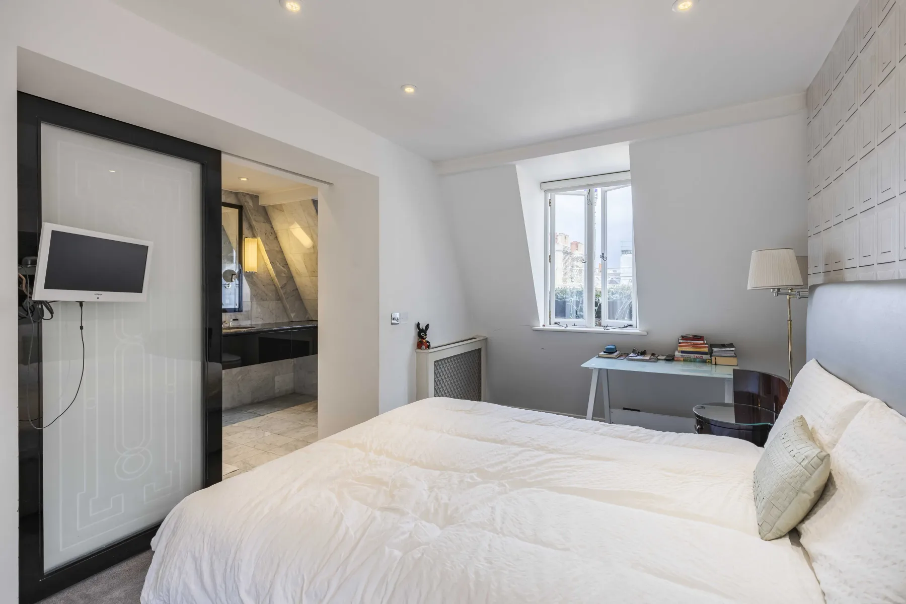 Un dormitorio luminoso con una cama grande y un escritorio junto a la ventana.