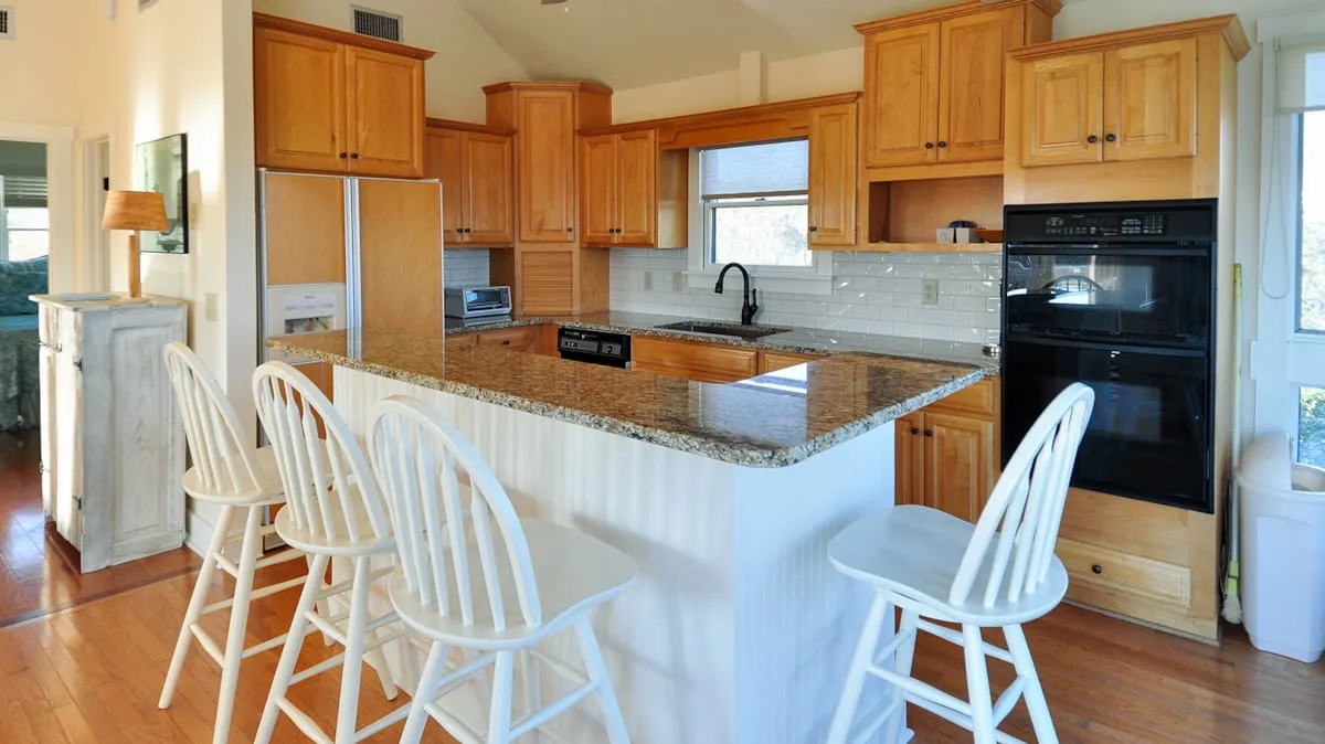 Una cocina luminosa con gabinetes de madera, una isla central y asientos blancos.