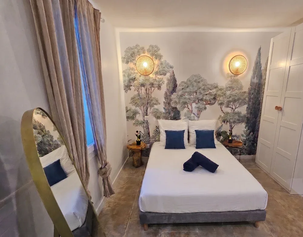 A bedroom with a bed, blue pillows, and a tree mural behind it.
