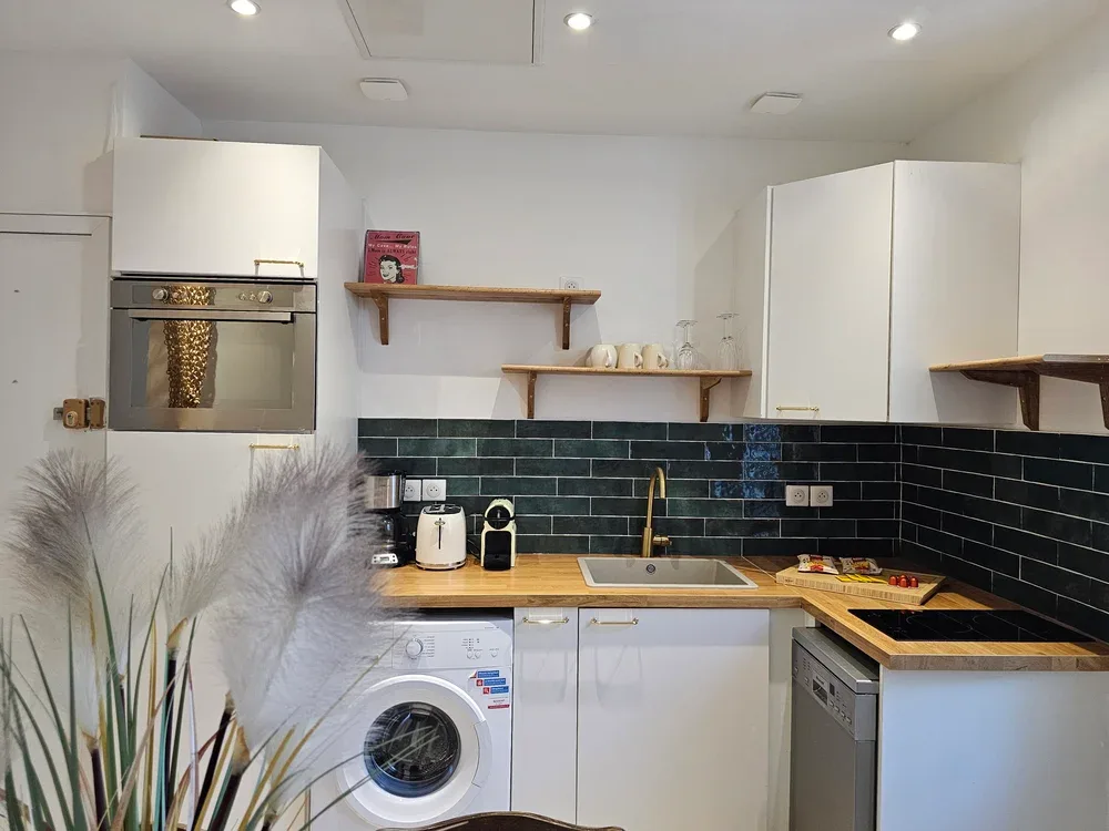 A compact kitchen with white cabinets, dark tile backsplash, and a washing machine.