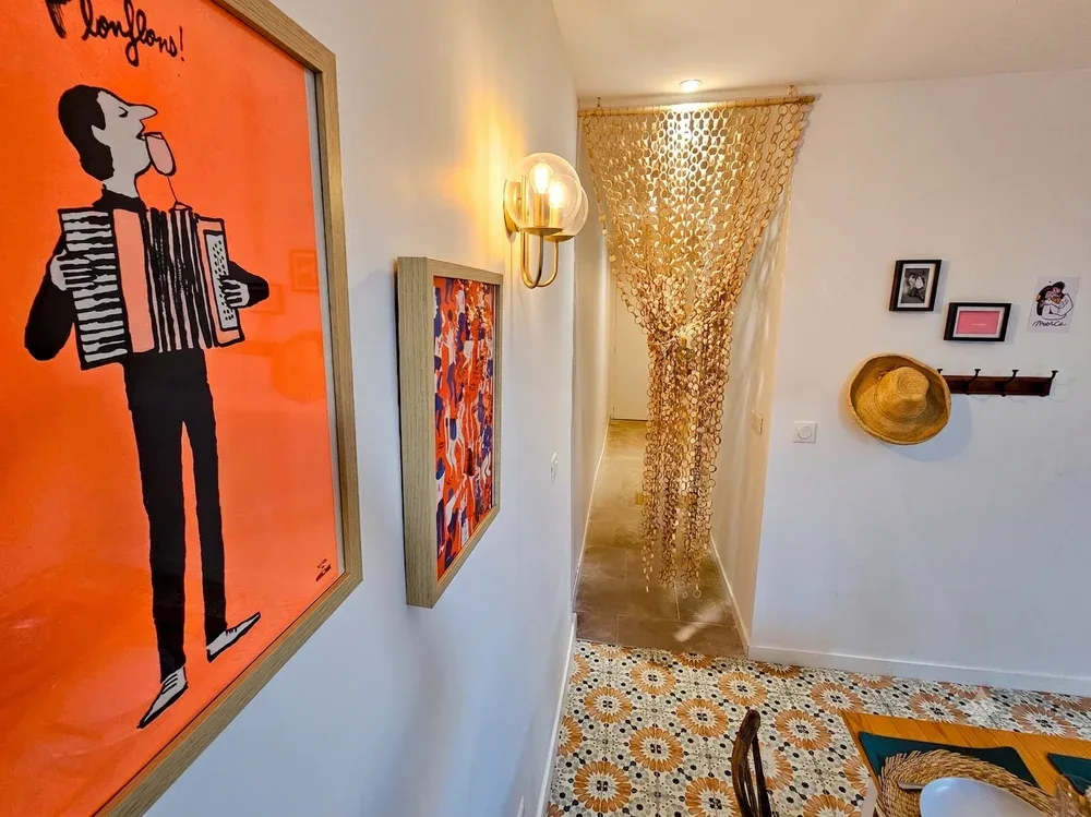 A hallway with colorful framed artwork and a gold-toned beaded curtain.