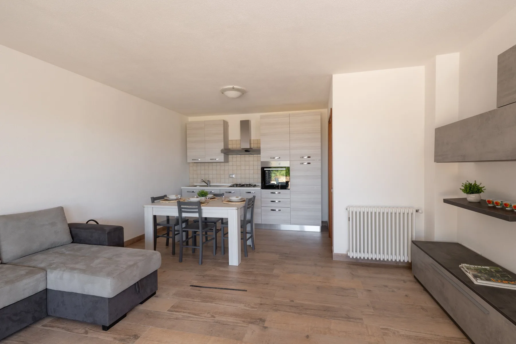 A living and dining area with a sectional sofa, table, and kitchen in the background.