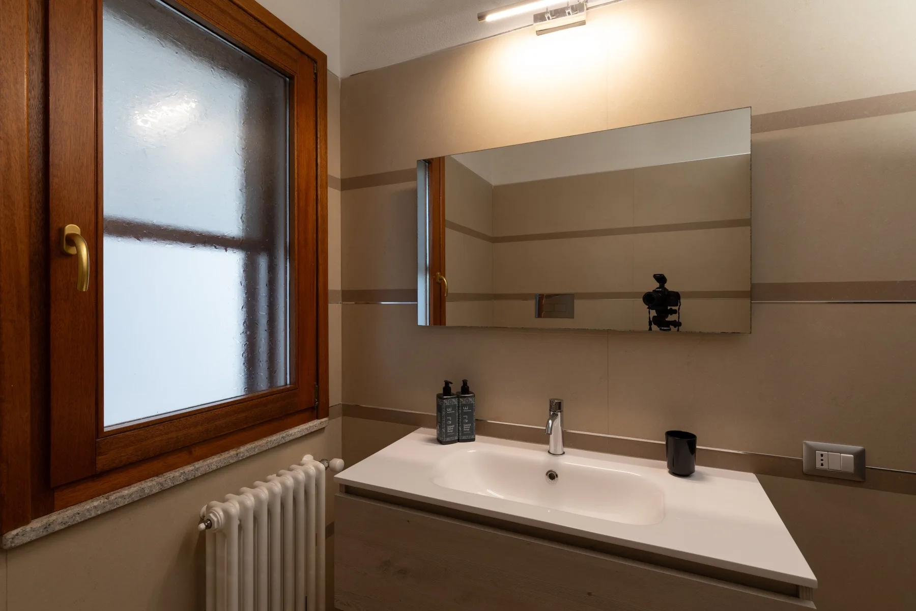 A bathroom vanity with a wide mirror, sink, and frosted window.