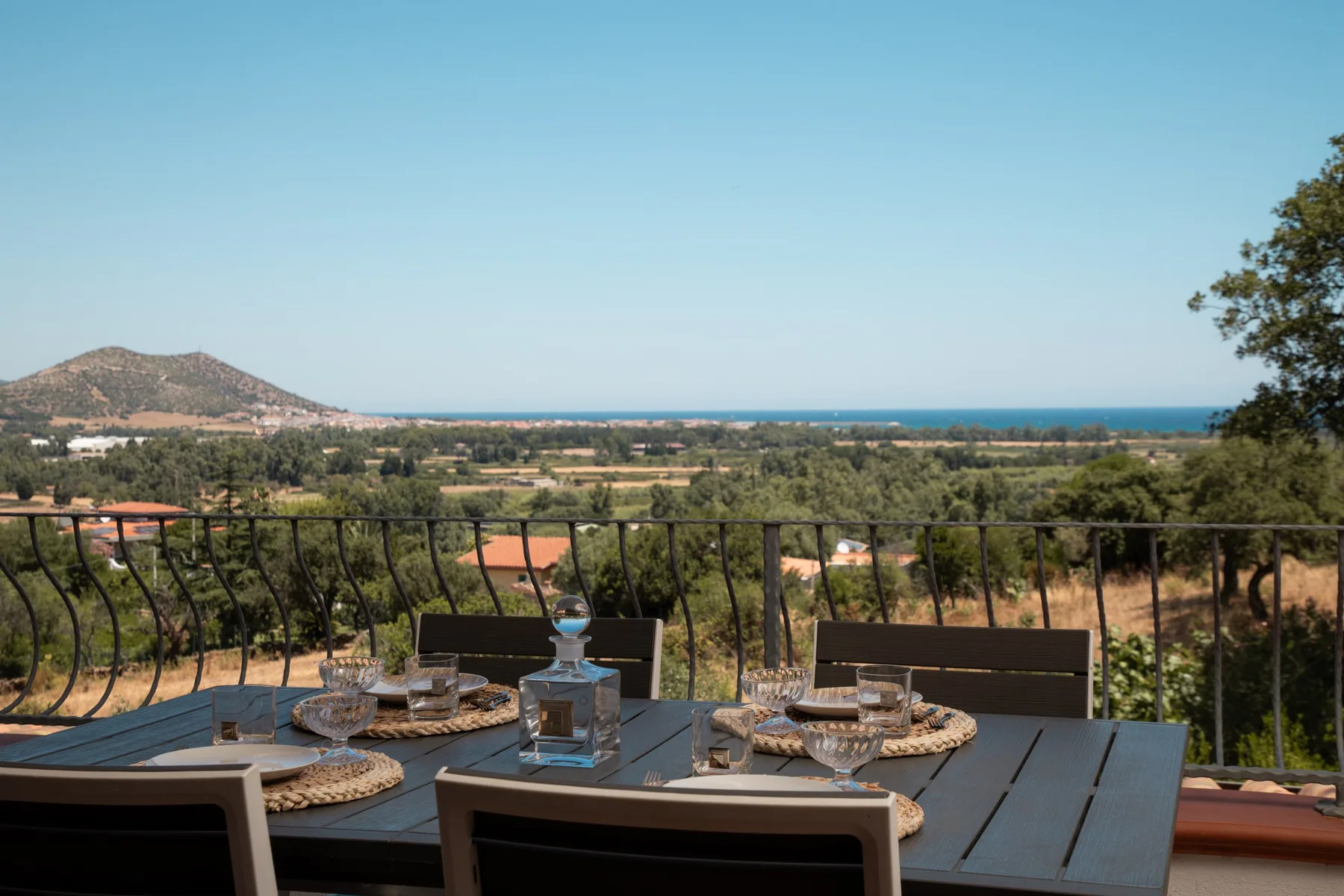 An outdoor dining table overlooks a green valley and the sea.