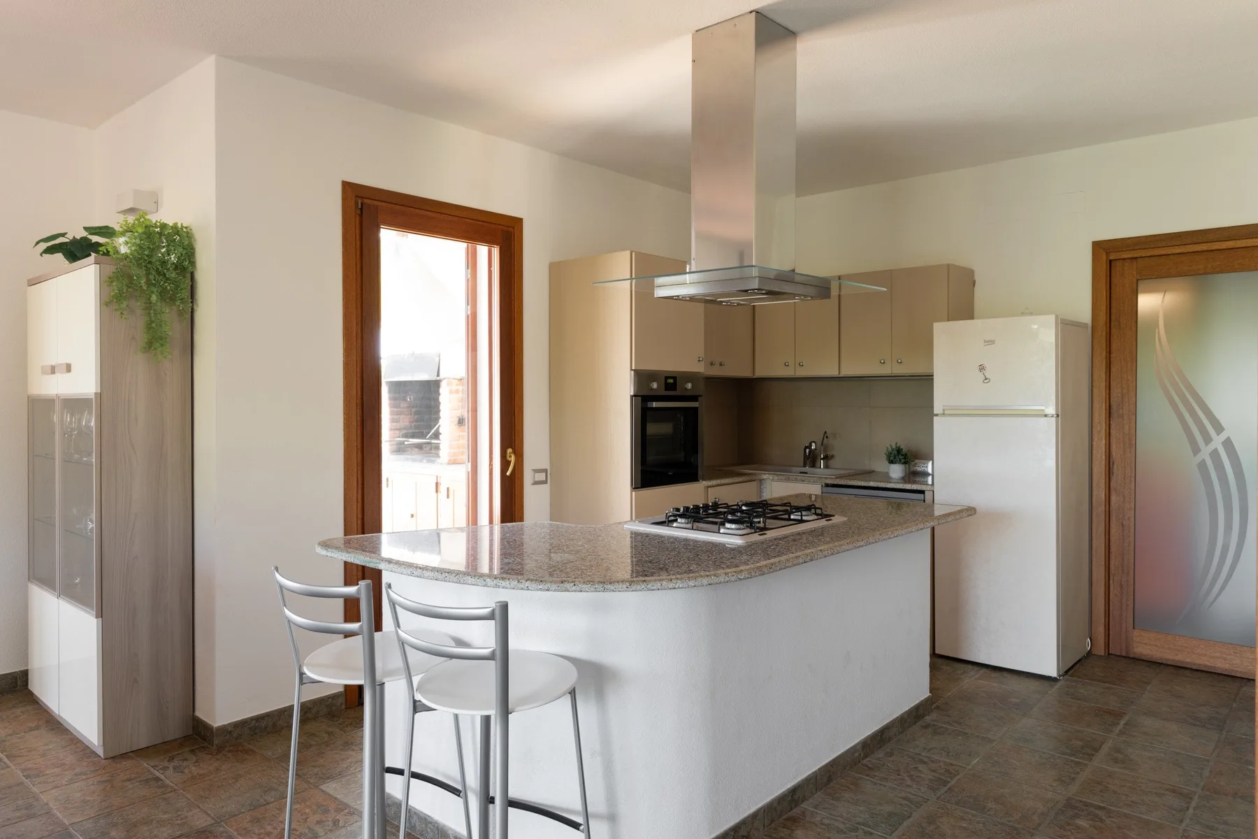 A bright kitchen with a curved island and metal bar stools.