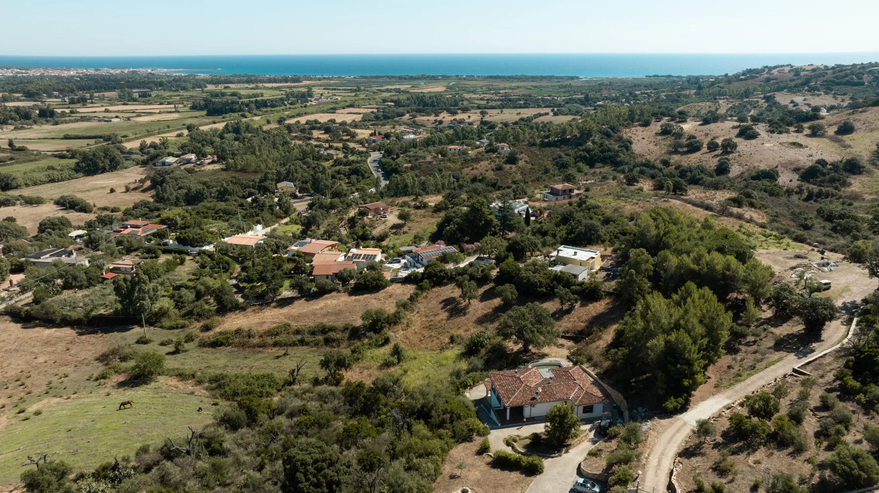 Aerial view of a rural landscape with scattered homes and the sea on the horizon.