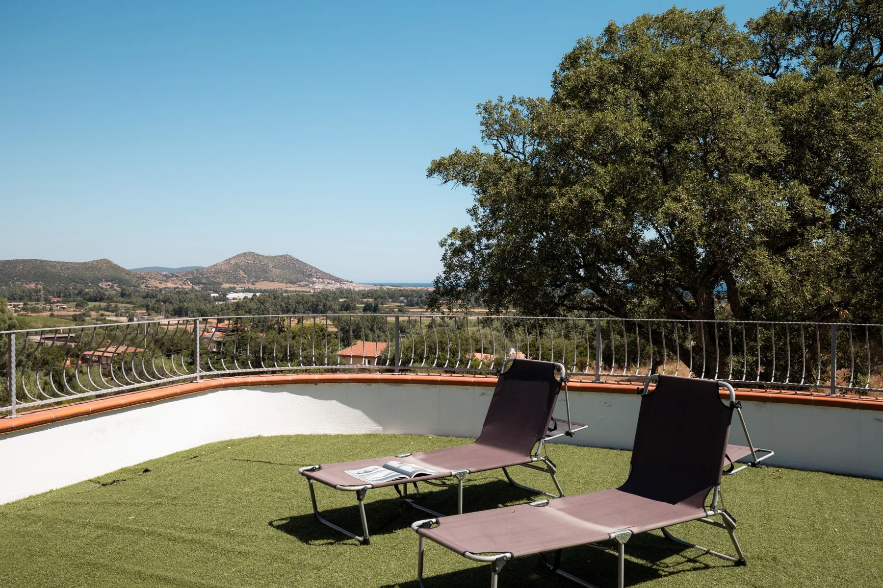 A rooftop terrace has reclining lounge chairs and a view of the surrounding hills.