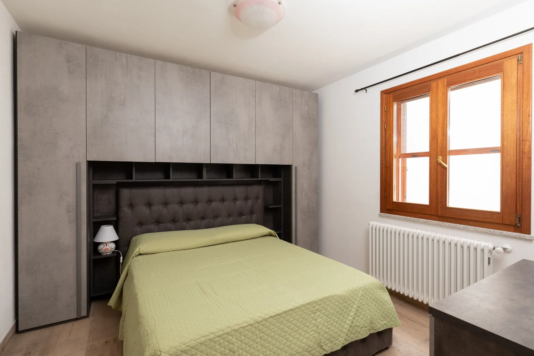 A bedroom with a bed beneath built-in shelving and a window.