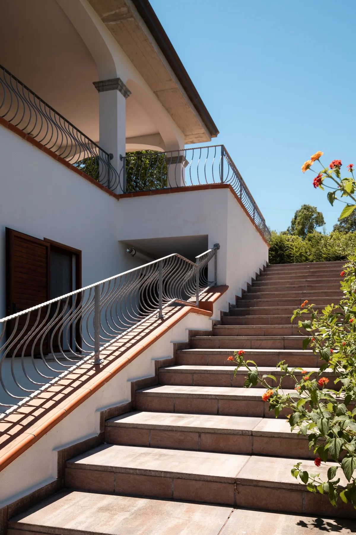 An outdoor staircase with metal railings rises beside a white building.