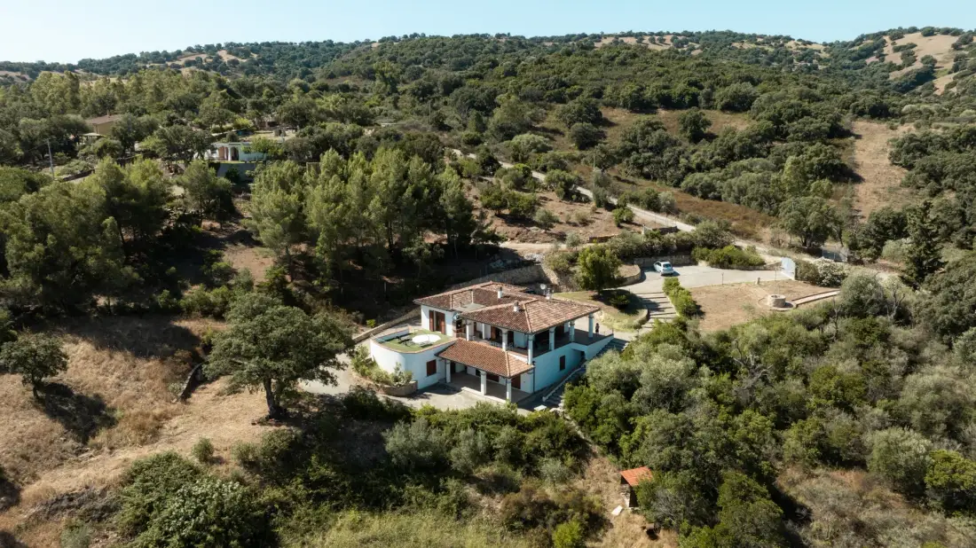 A house sits among trees and dry, rolling hills.