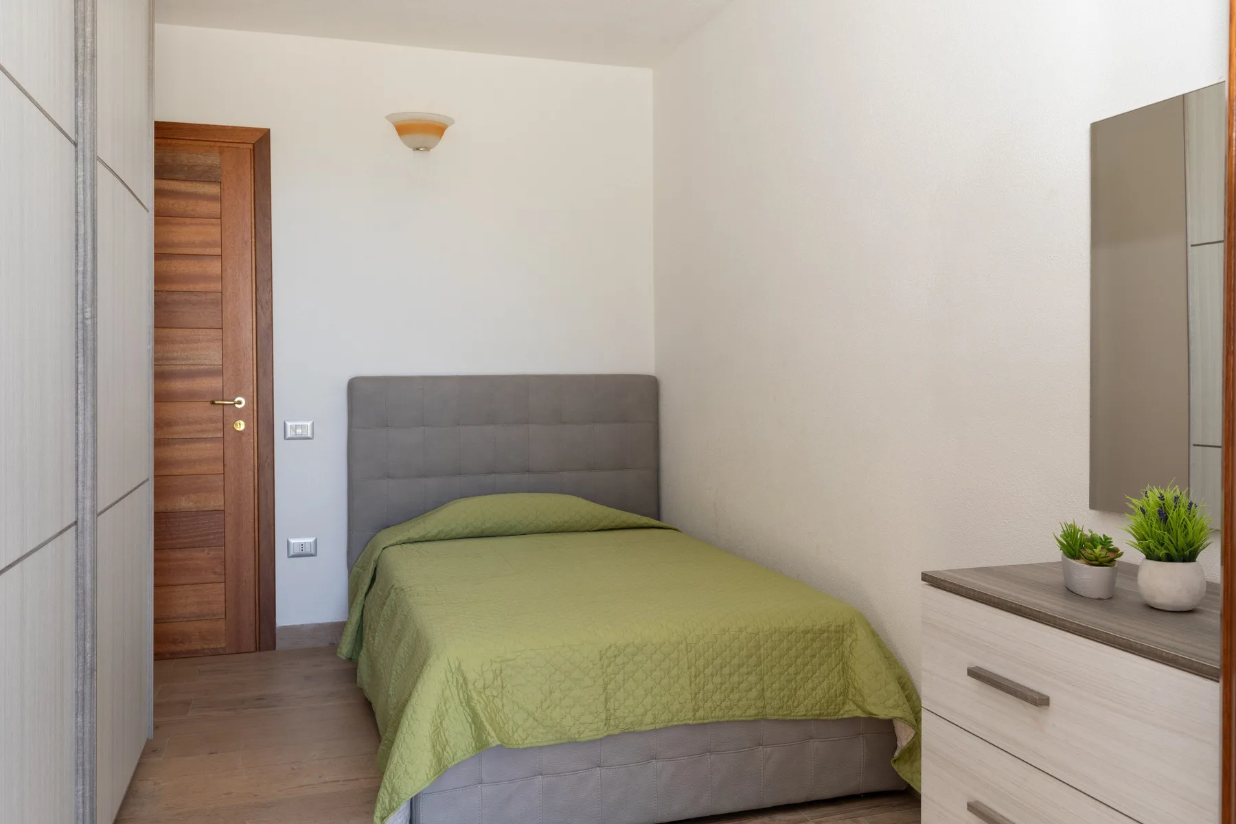 A bedroom with a bed covered by a green bedspread and a wooden door.