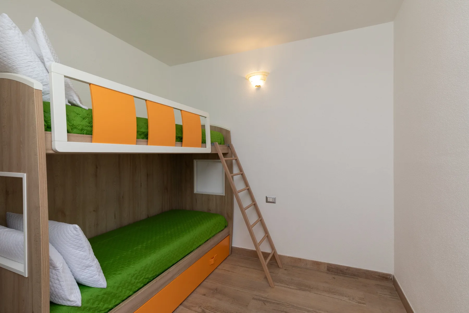 A bunk-bed room with orange guard panels, green bedding, and a wooden ladder.