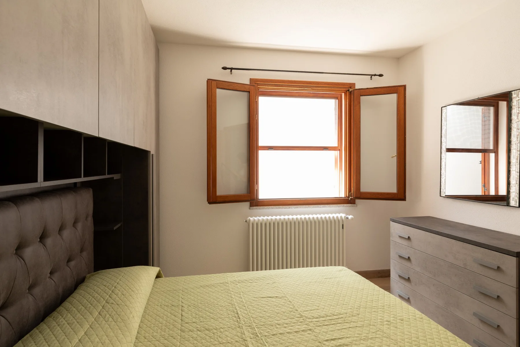 A bedroom with a bed, a window, and a radiator.