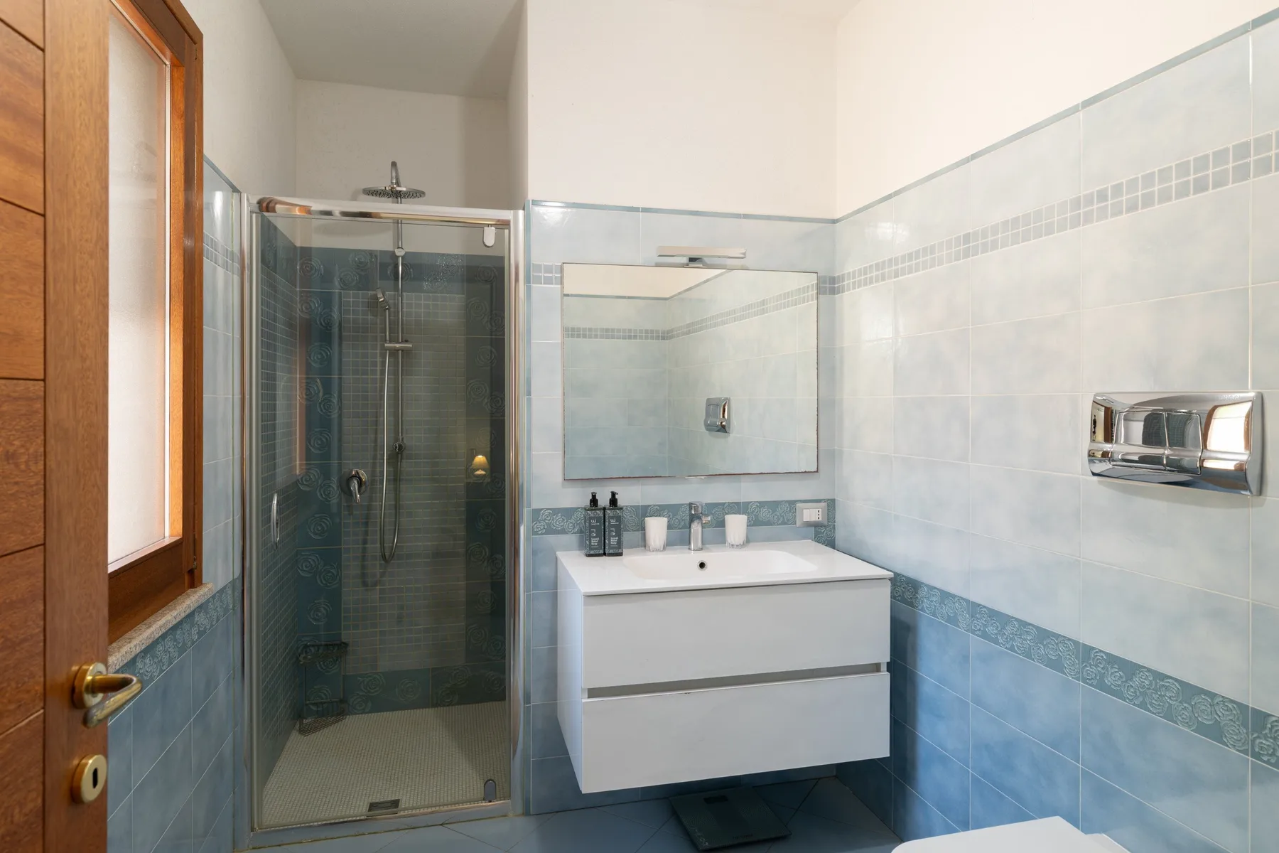 A tiled bathroom with a glass shower and a wall-mounted sink cabinet.