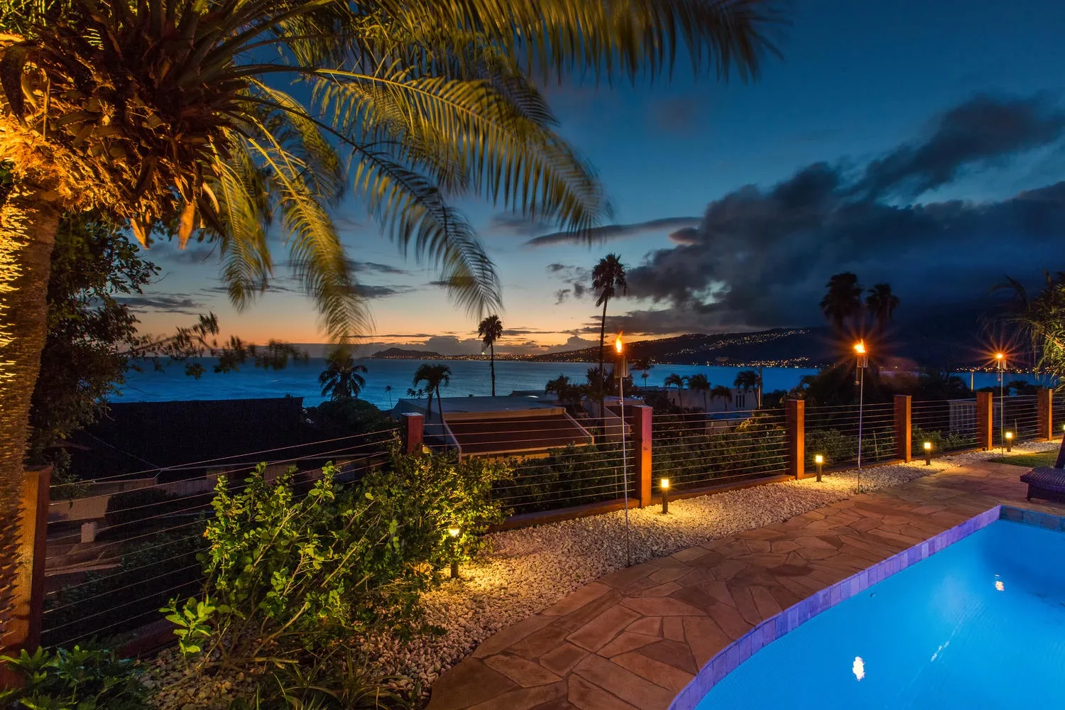 Una terraza iluminada junto a la piscina mira hacia el agua al anochecer.