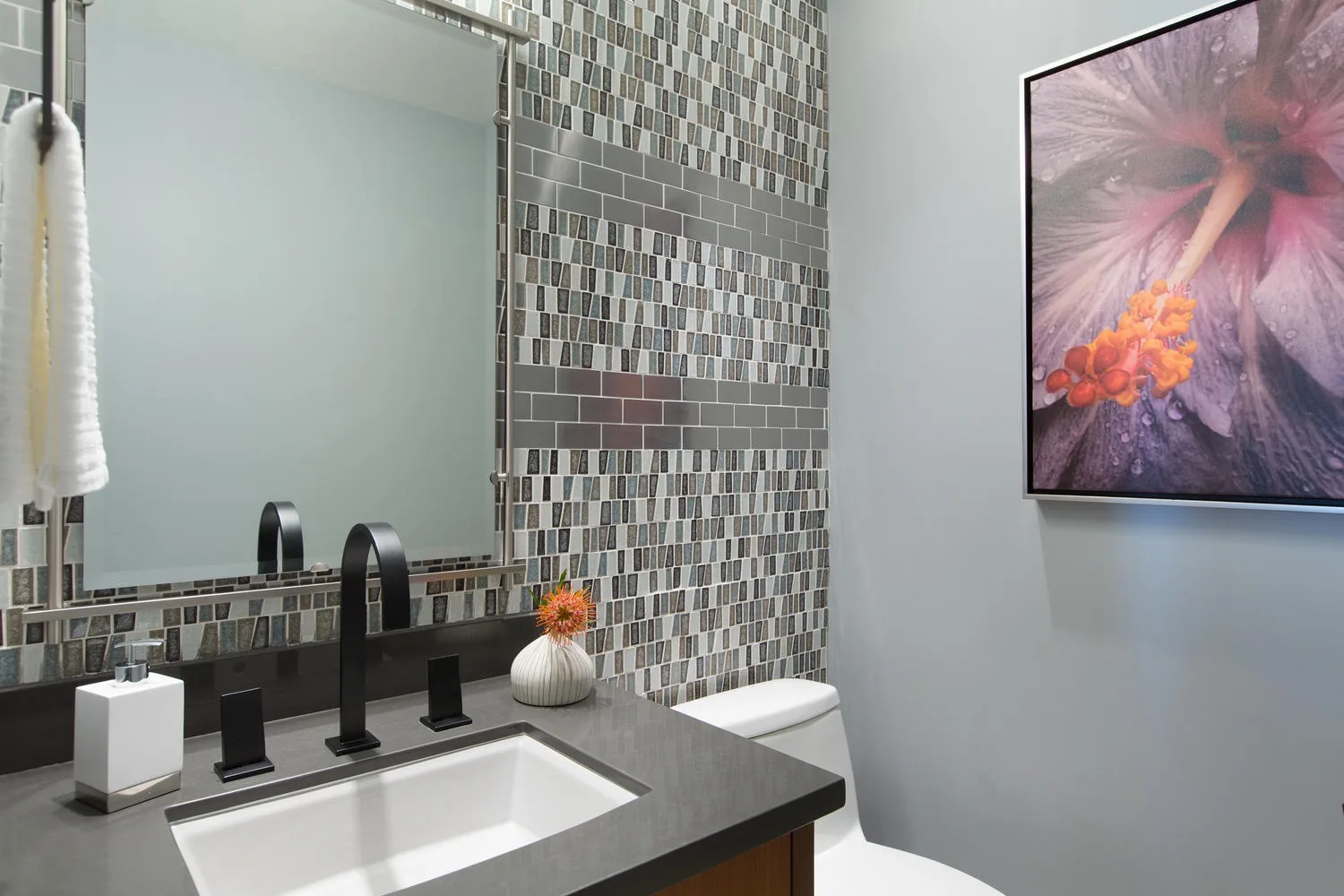 Un tocador de baño con lavabo, grifo oscuro y pared de azulejos.