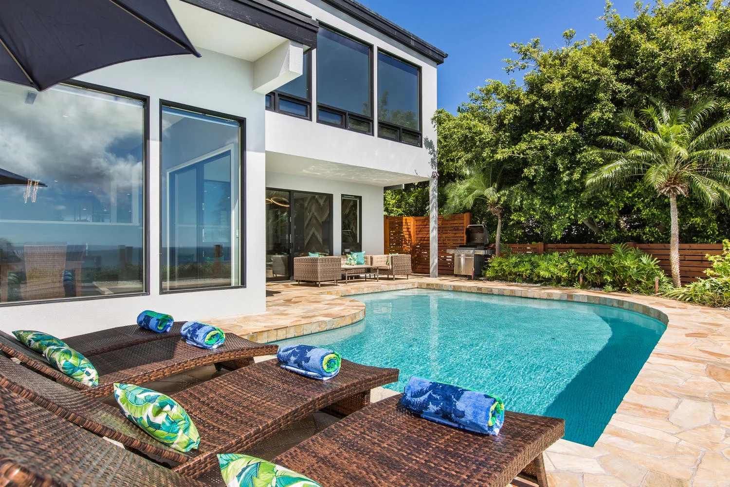 Una piscina junto a una casa blanca moderna, con tumbonas en el patio.