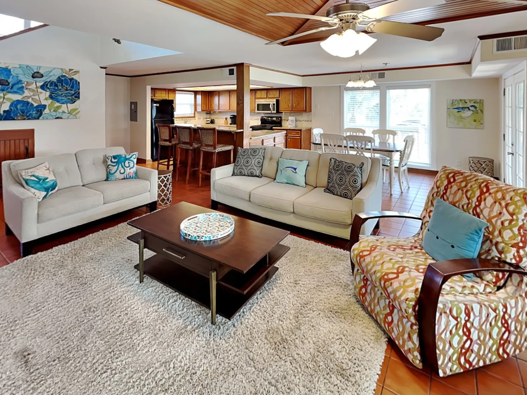 A living room with seating around a coffee table, with the kitchen and dining area beyond.