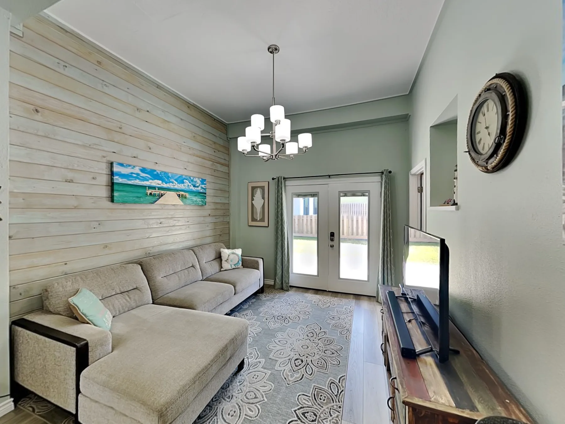 A living room with a sectional sofa, a television, and double glass doors.