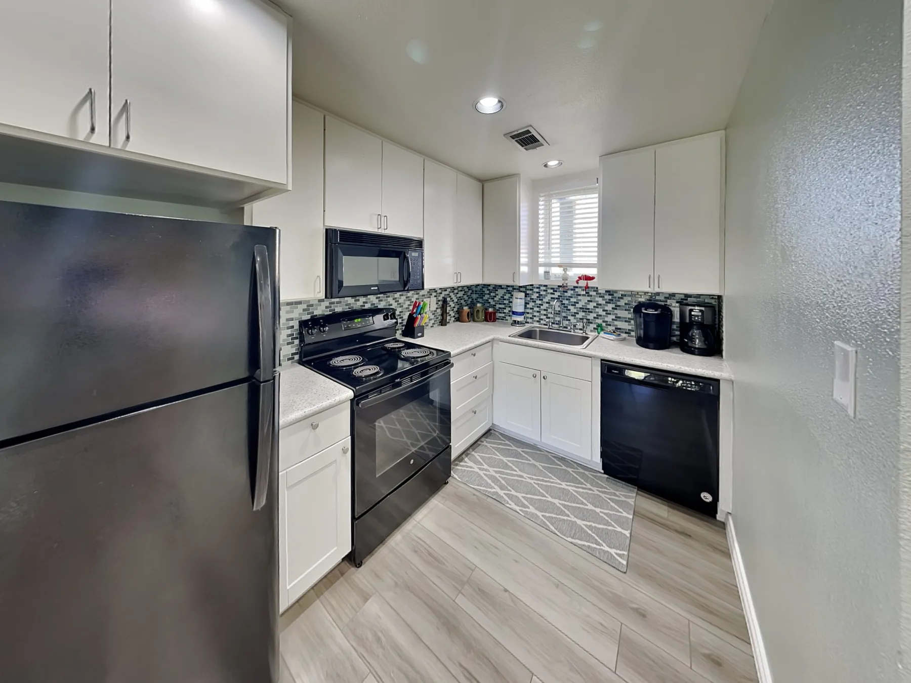 A bright kitchen with white cabinets, dark appliances, and a patterned backsplash.