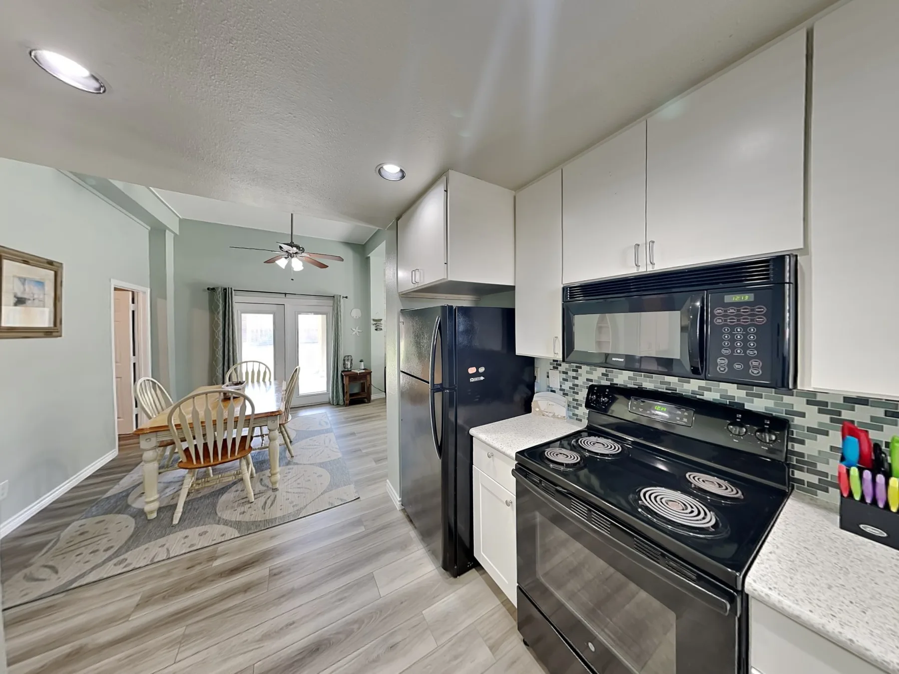 A kitchen with dark appliances opens into a dining area with a table and chairs.