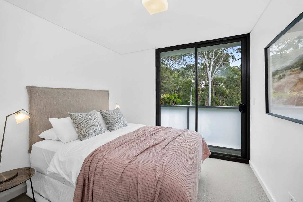 A bright bedroom with a neatly made bed beside a large glass door.