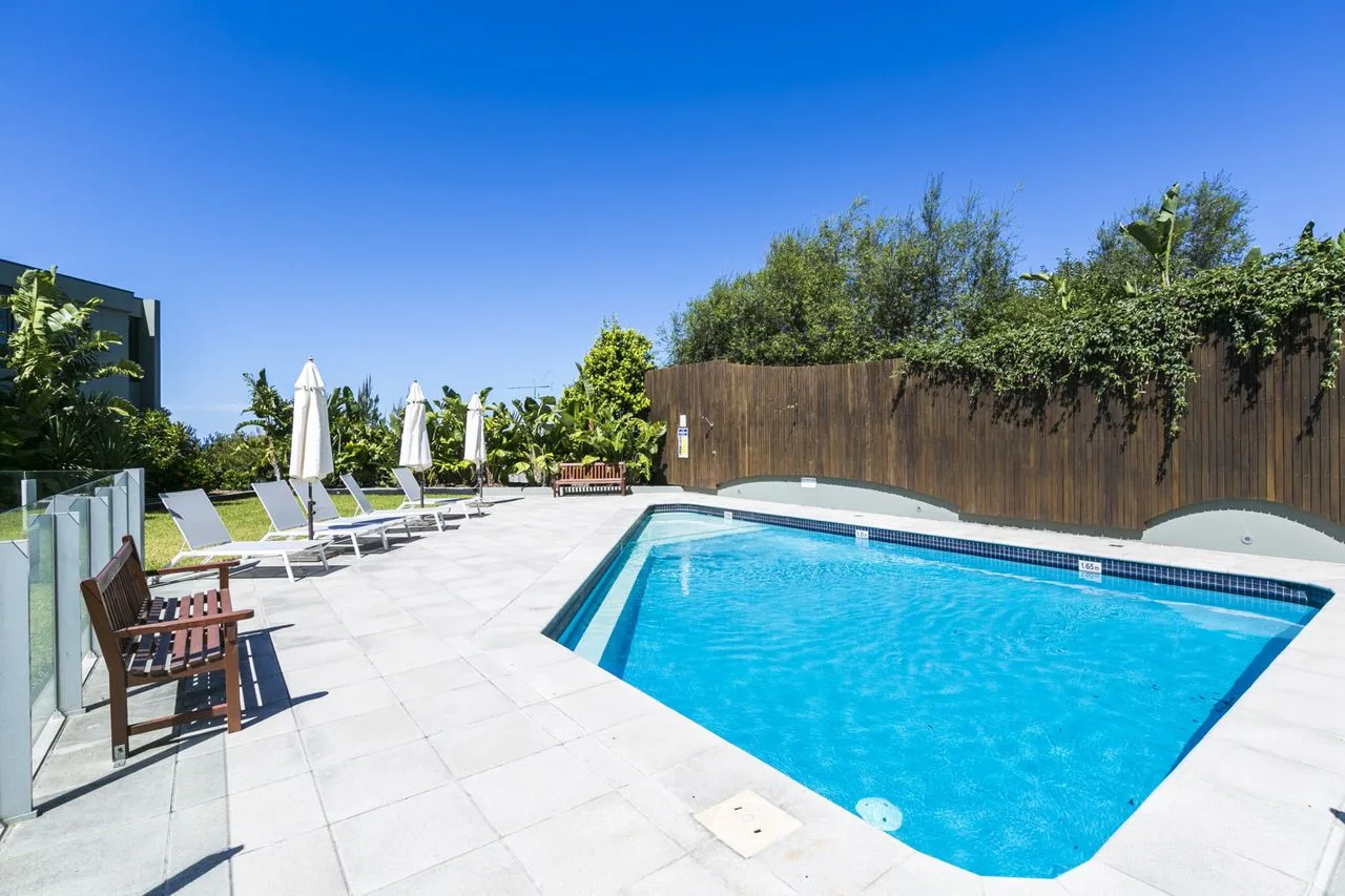 An outdoor swimming pool is surrounded by a paved deck and lounge seating.