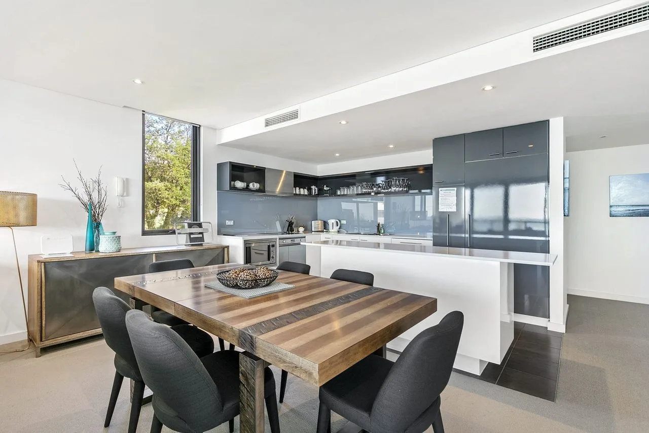 A modern kitchen and dining area with a large wooden table and dark cabinetry.
