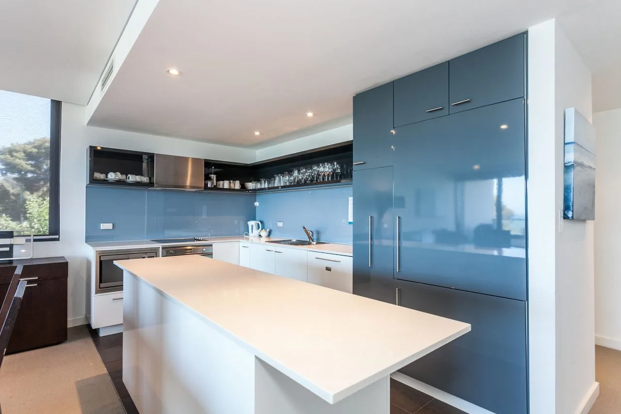 A modern kitchen with blue cabinetry, stainless steel appliances, and a large island.