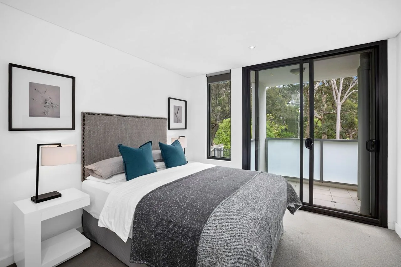 A bedroom with a bed beside sliding glass doors opening onto a balcony.