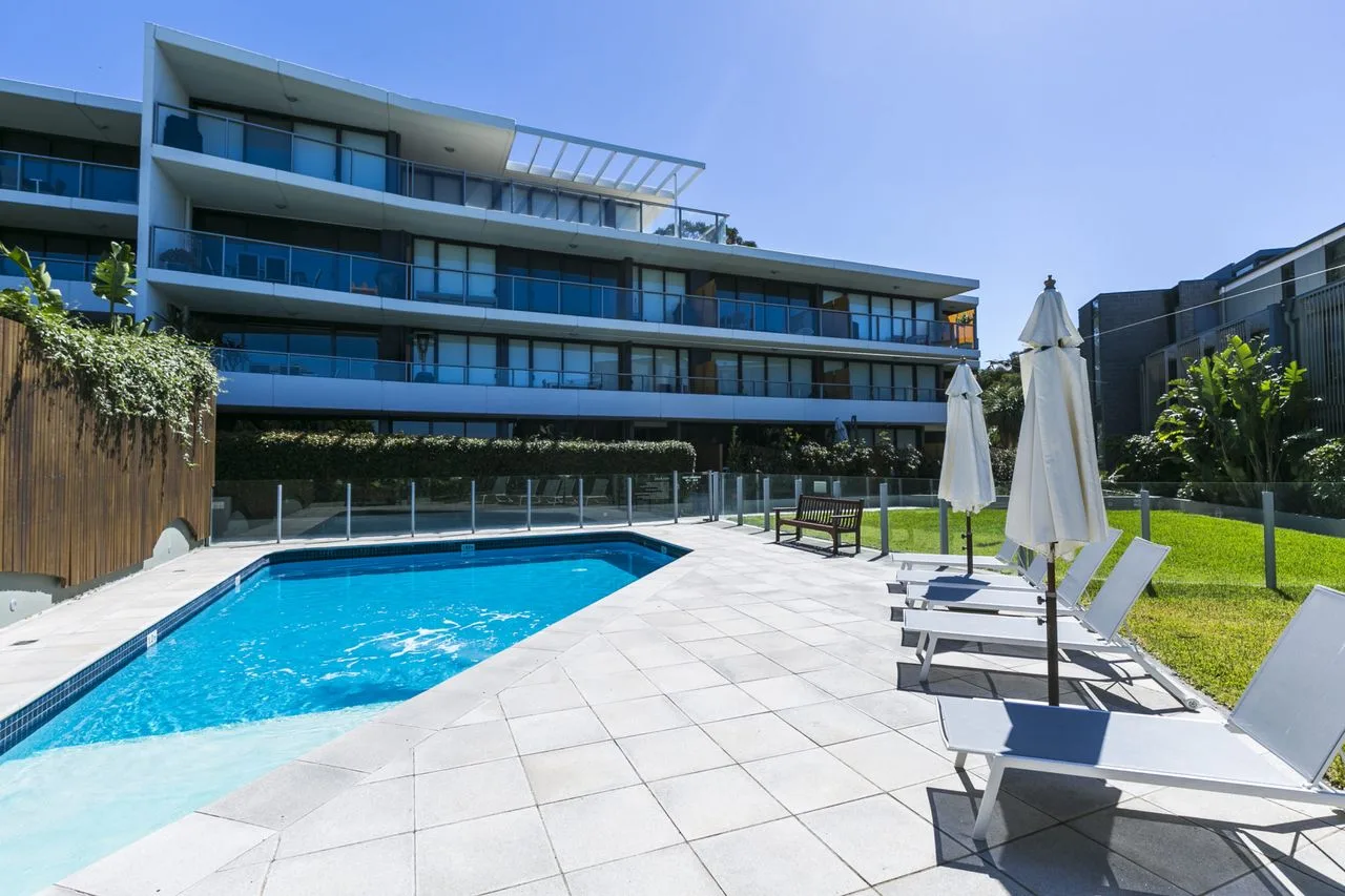 An outdoor pool and paved patio with lounge seating beside a modern building.