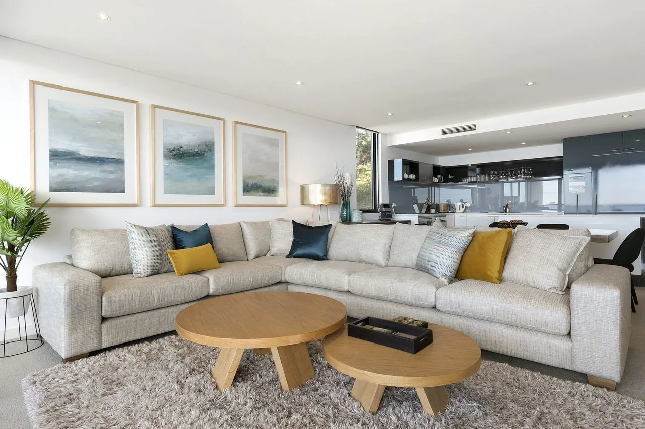 A bright living room with a large sectional seating area and round coffee tables.