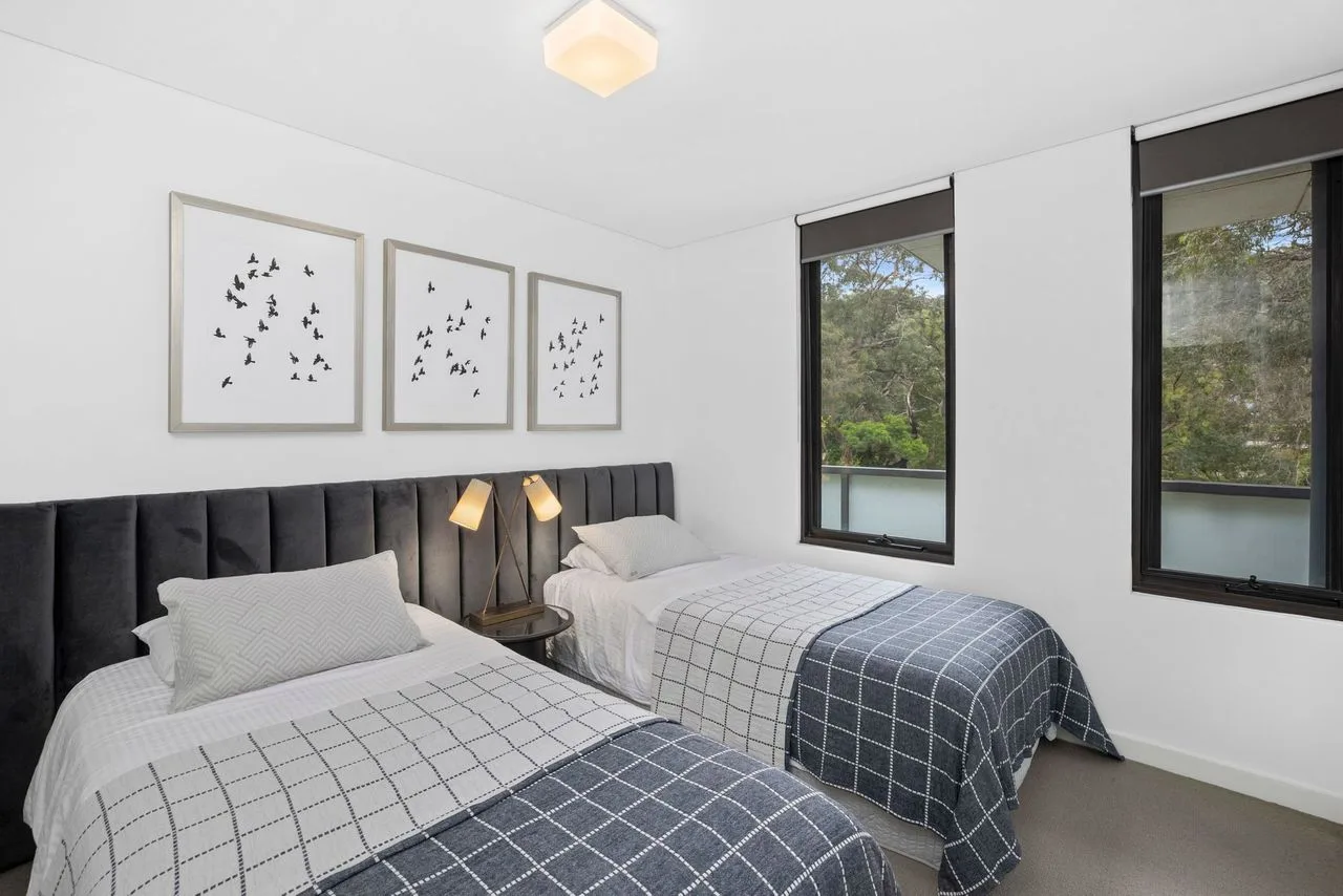 A bedroom with two single beds, bedside lamps, and large windows.