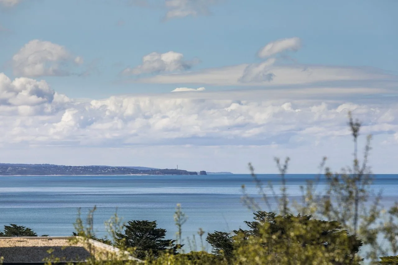 A coastal view across calm blue water beneath a partly cloudy sky.