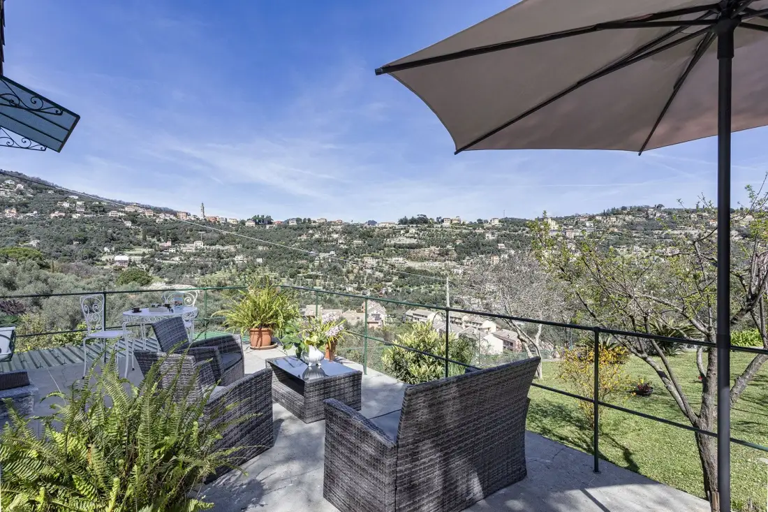 Una terraza exterior con asientos ofrece vistas a una ladera verde y casas dispersas.
