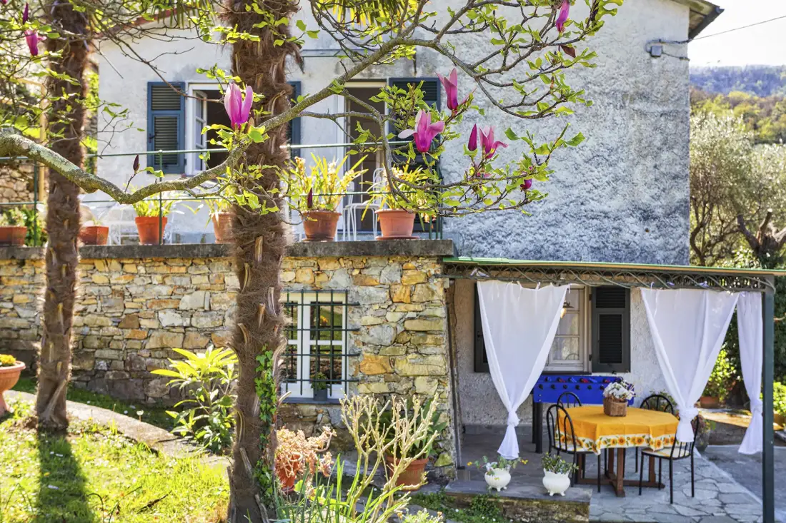 Una casa de piedra con una zona de estar exterior con cortinas y árboles en flor.