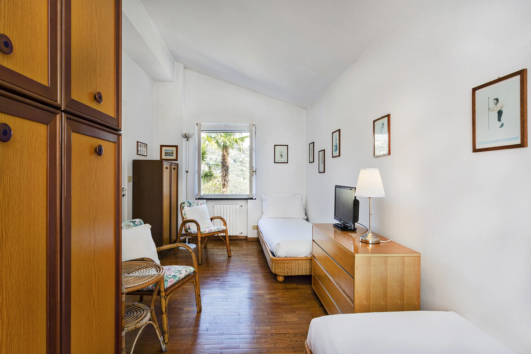 Un dormitorio luminoso con camas individuales, asientos de mimbre y una ventana.